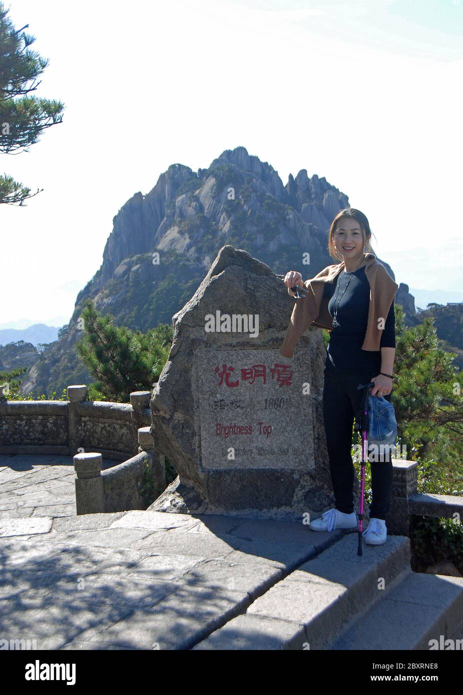 Huangshan Mountain in Anhui Province, China. Tourist photographed at the summit marker of Brightness Top. Lotus Peak, the highest peak, is behind Stock Photo