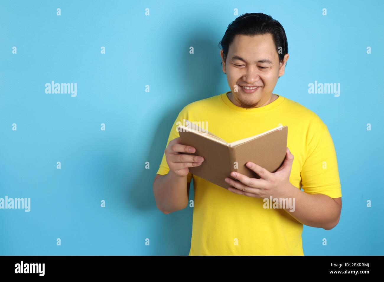 Portrait of Asian man wearing casual white shirt looked happy and smiling while reading a book Stock Photo