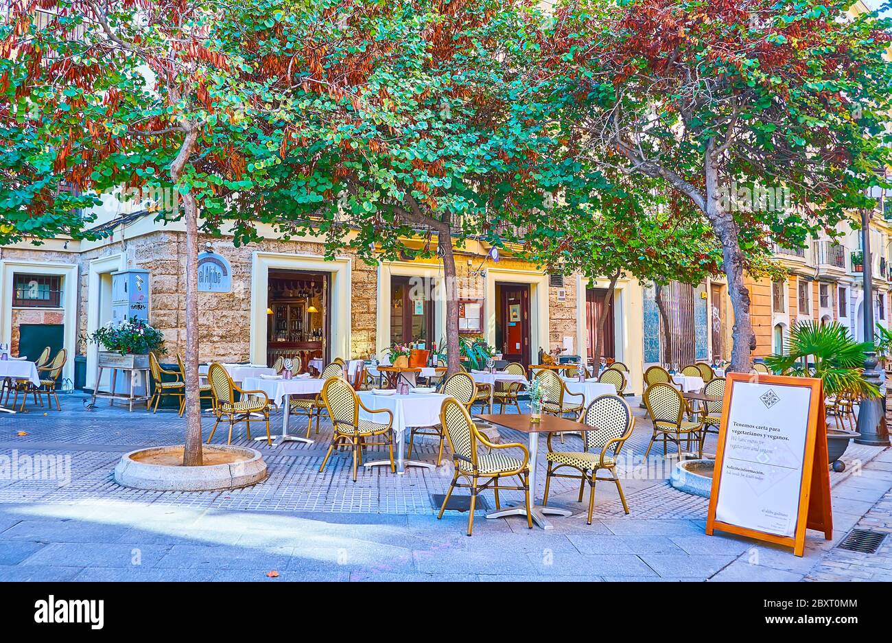 CADIZ, SPAIN - SEPTEMBER 23, 2019: The cozy outdoor terrace of the restaurant with small tables under the shady trees of Calle Plocia street in old to Stock Photo