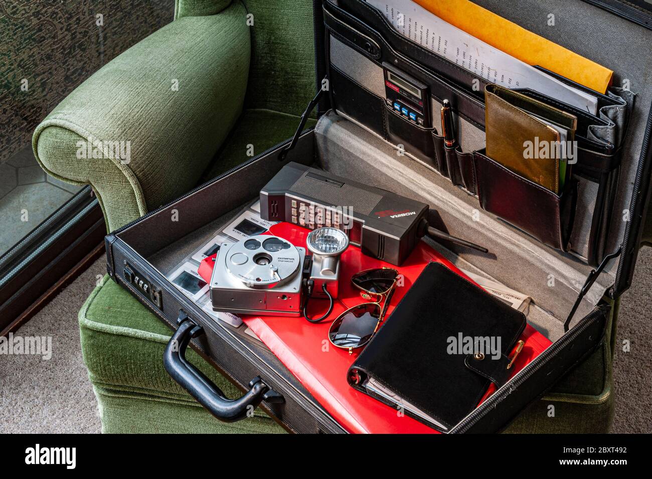 1980's technology items in briefcase incl. Mobira Cityman mobile phone,  Olympus O 35mm camera, Filofax diary, aviator sunglasses, cheque book & chair Stock Photo