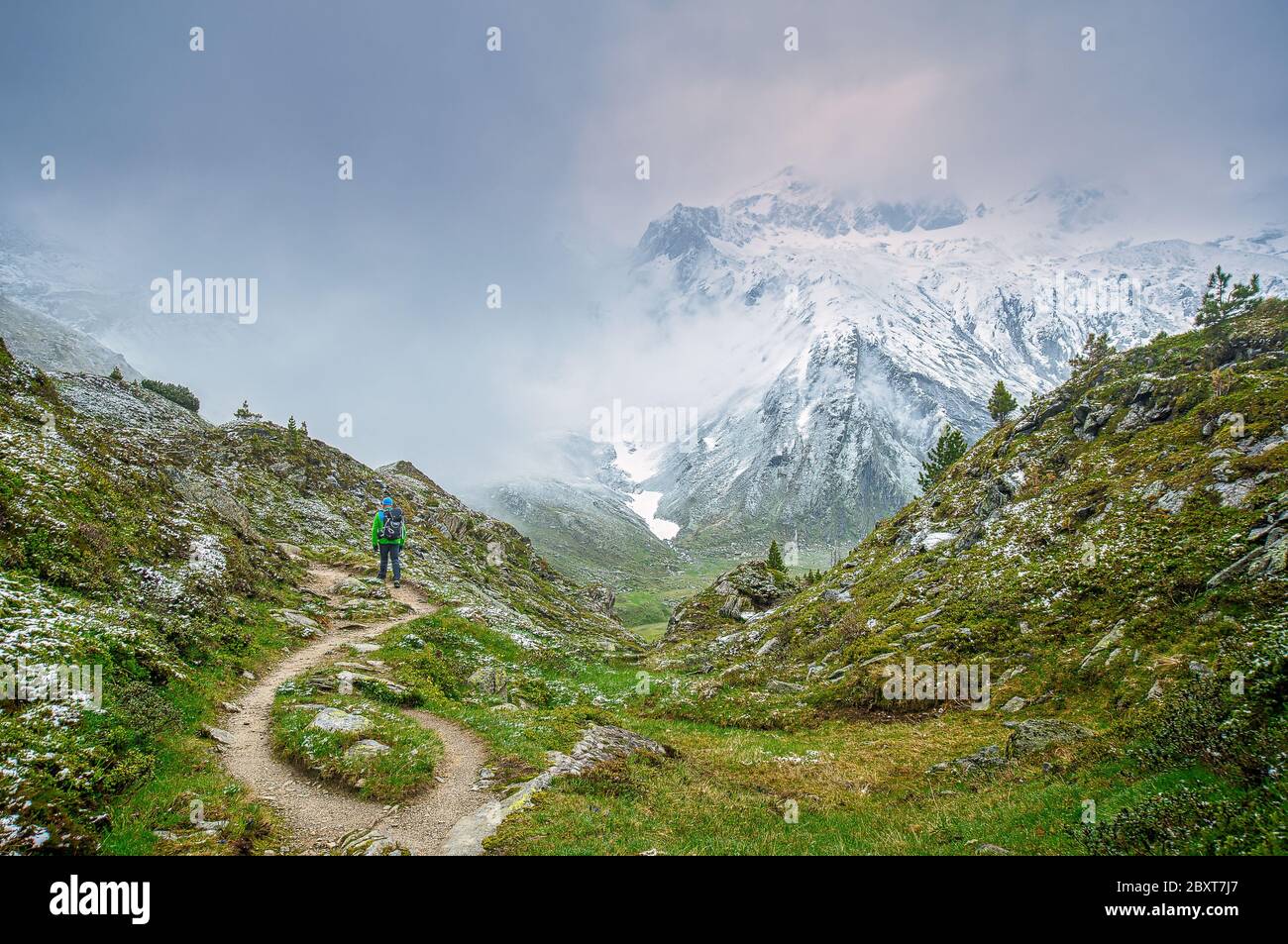 Foggy view at a mountain scenery in the austrian alps. A hiker from behind is watching at the snowy peak far away through the fog Stock Photo
