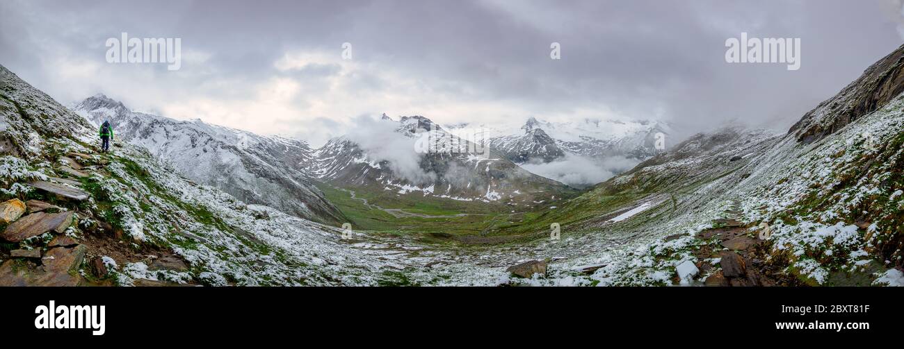 Panoramic photo of a hiker who is walking up a snow covered hillside with a beautiful mounitain in the foggy background Stock Photo