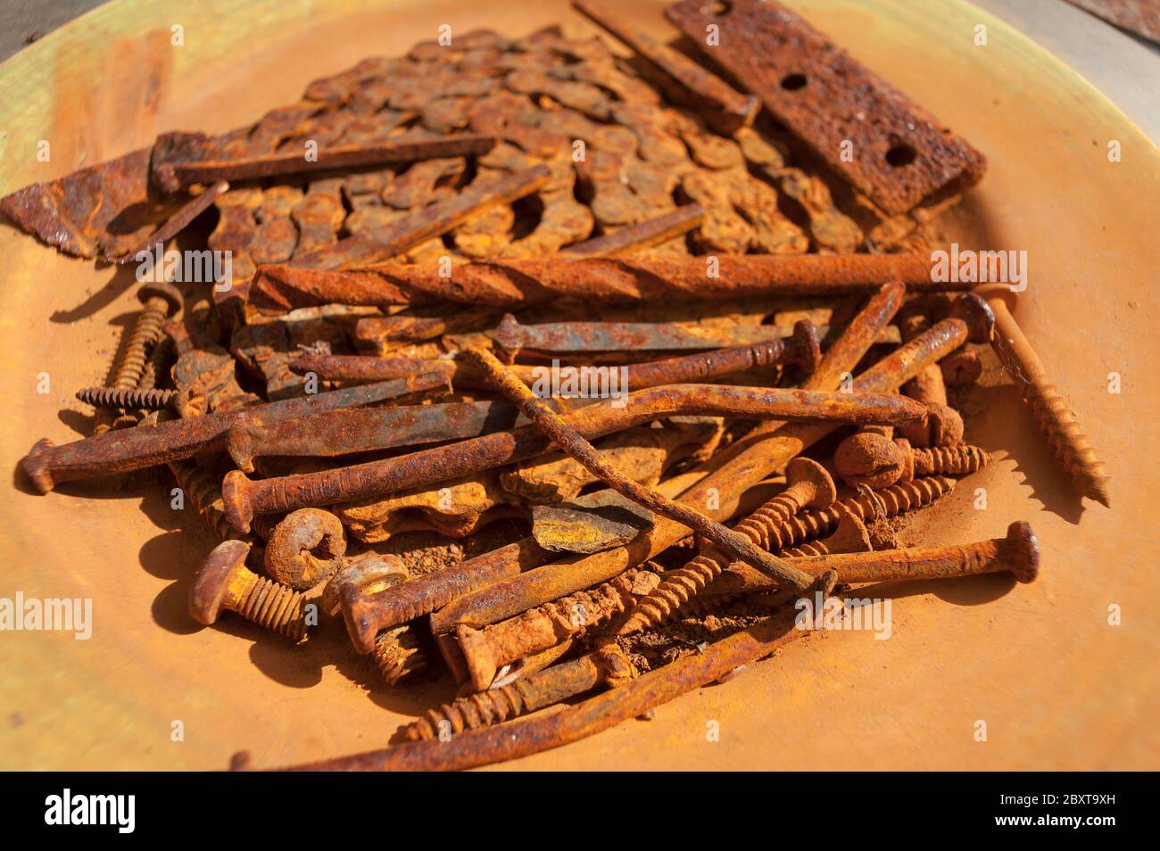 Pile of iron and steel nails, screws, metal and chain left to rust in outside plate showing rusty brown orange stains Stock Photo
