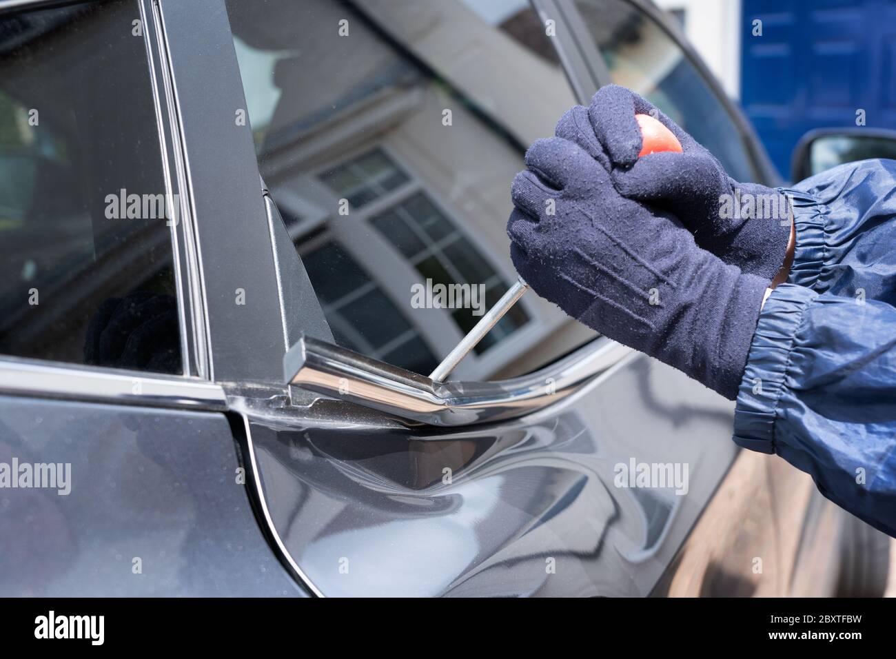 Thief attempting to break into a car with a screwdriver and damaging the car's bodywork in the process. Hertfordshire. UK Stock Photo