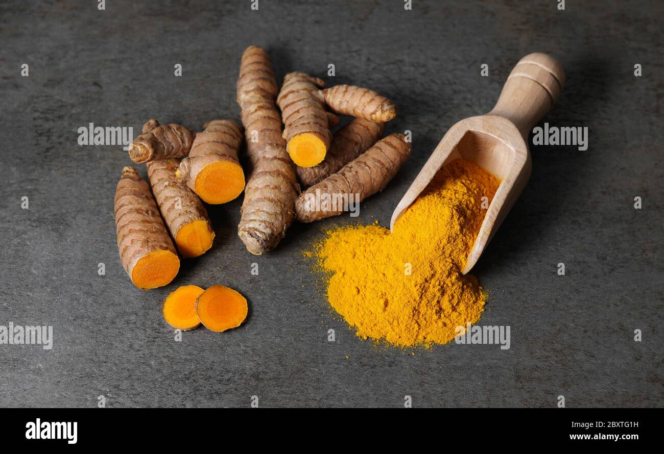 Turmeric powder healthy spice Asian food close up top view of turmeric root sliced and a wooden bailer on a rustic dark grey kitchen board. Stock Photo