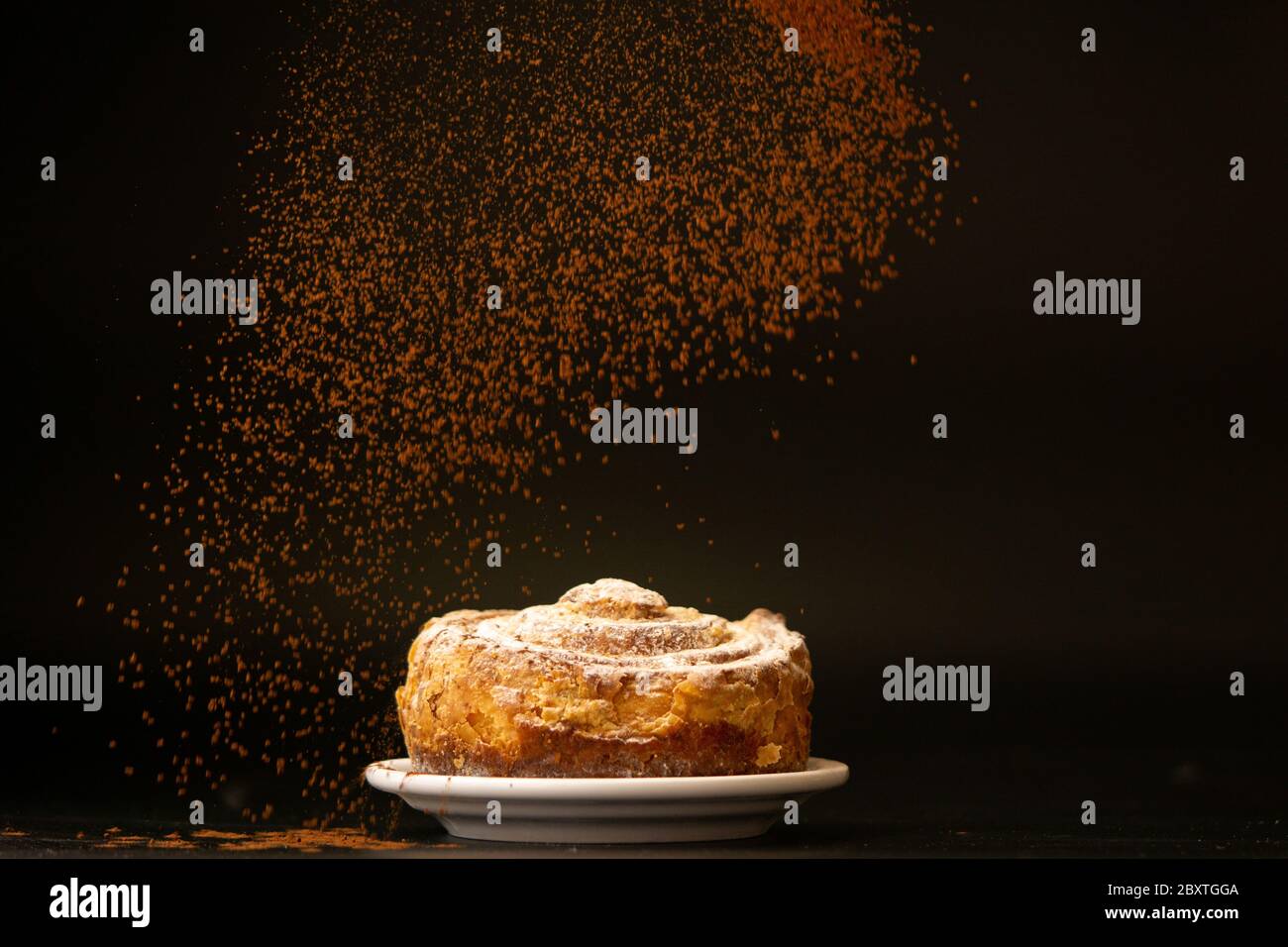 Cinnamon is sprinkling over fresh bundt cake. Cinnamon falls down, freezing motion. Copy space, black background. Bakery concept.  Stock Photo