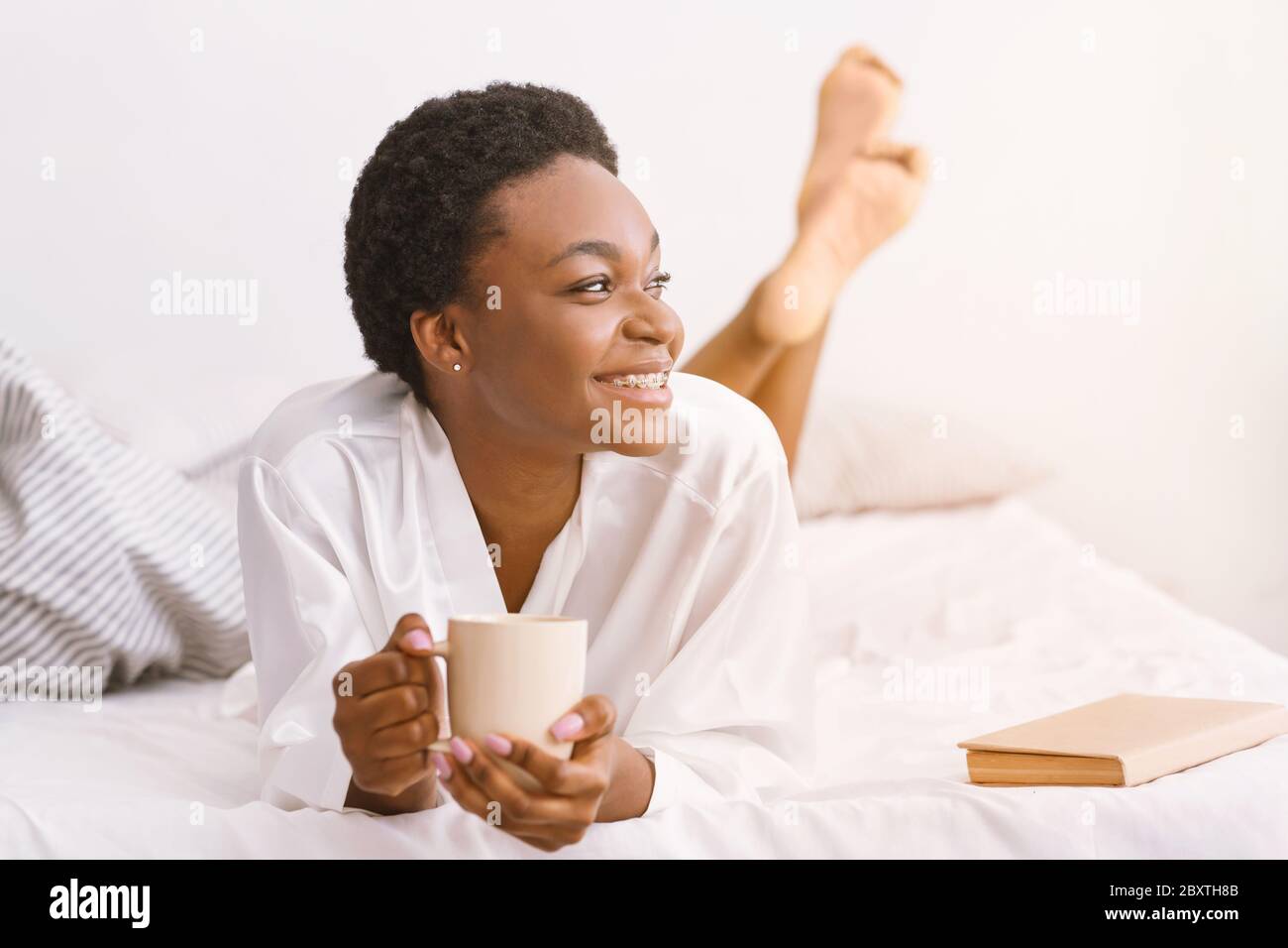 Good morning in comfortable bed. Smiling african american girl holding cup of coffee Stock Photo