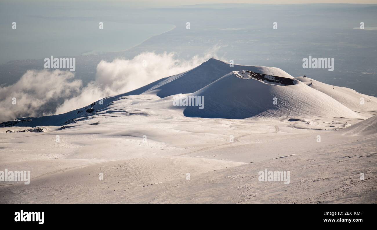 Cratere del vulcano Etna nel paesaggio innevato con nuvole e il golfo di Catania da sfondo Stock Photo
