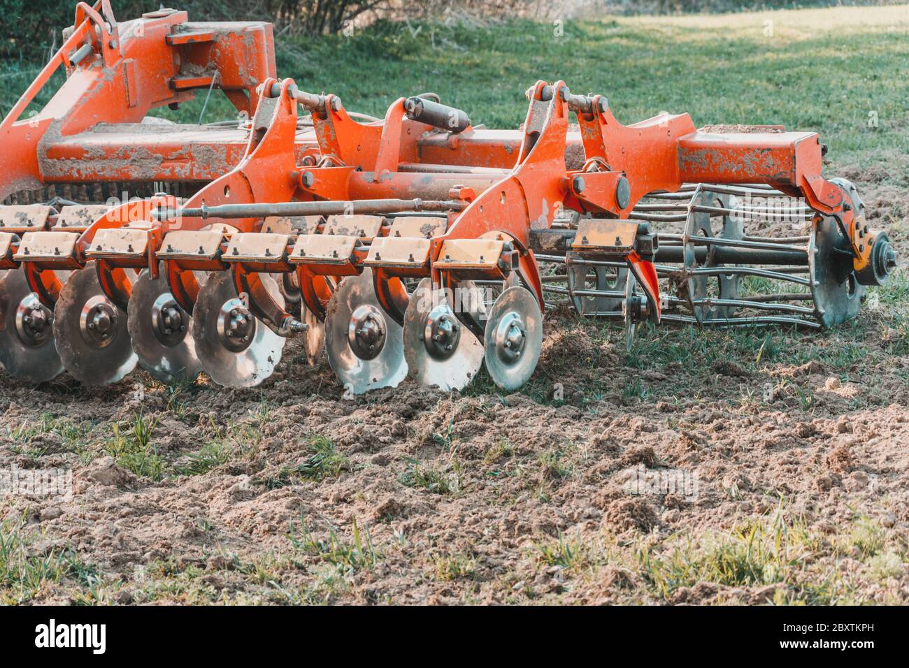 A red modern harrow stands in a field before sowing. Hydraulic mechanism for grinding the soil