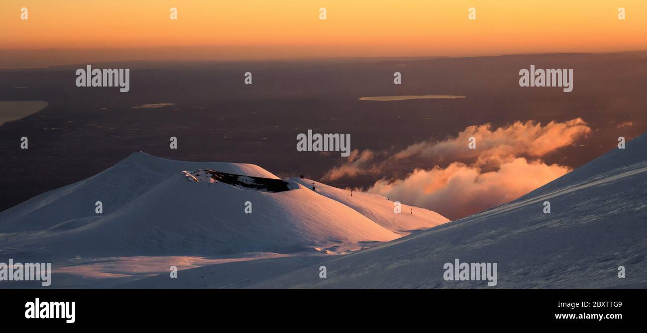 Cratere del vulcano Etna nel paesaggio innevato con nuvole e il golfo di Catania da sfondo al tramonto Stock Photo