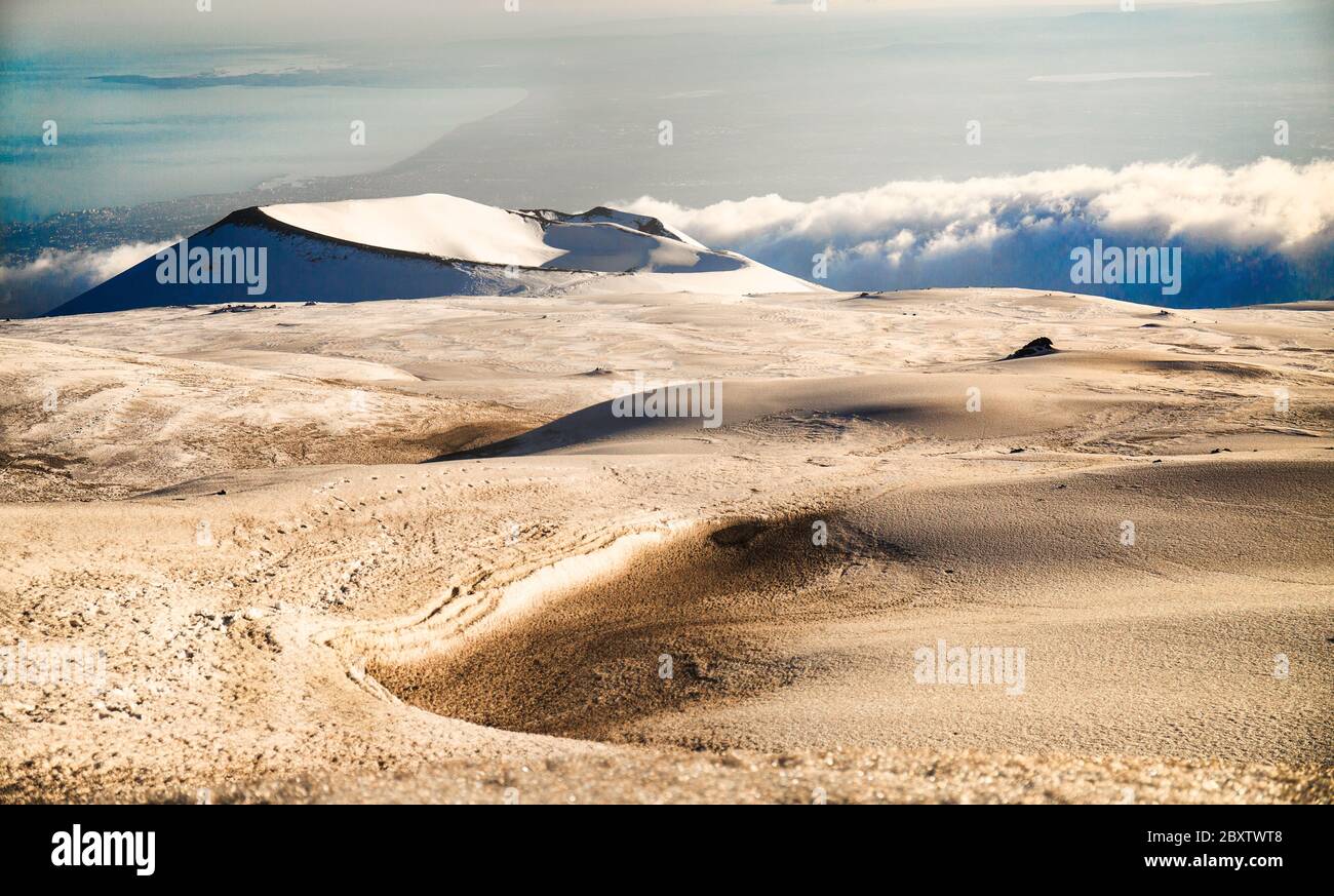 Cratere del vulcano Etna nel paesaggio innevato con nuvole e il golfo di Catania da sfondo Stock Photo