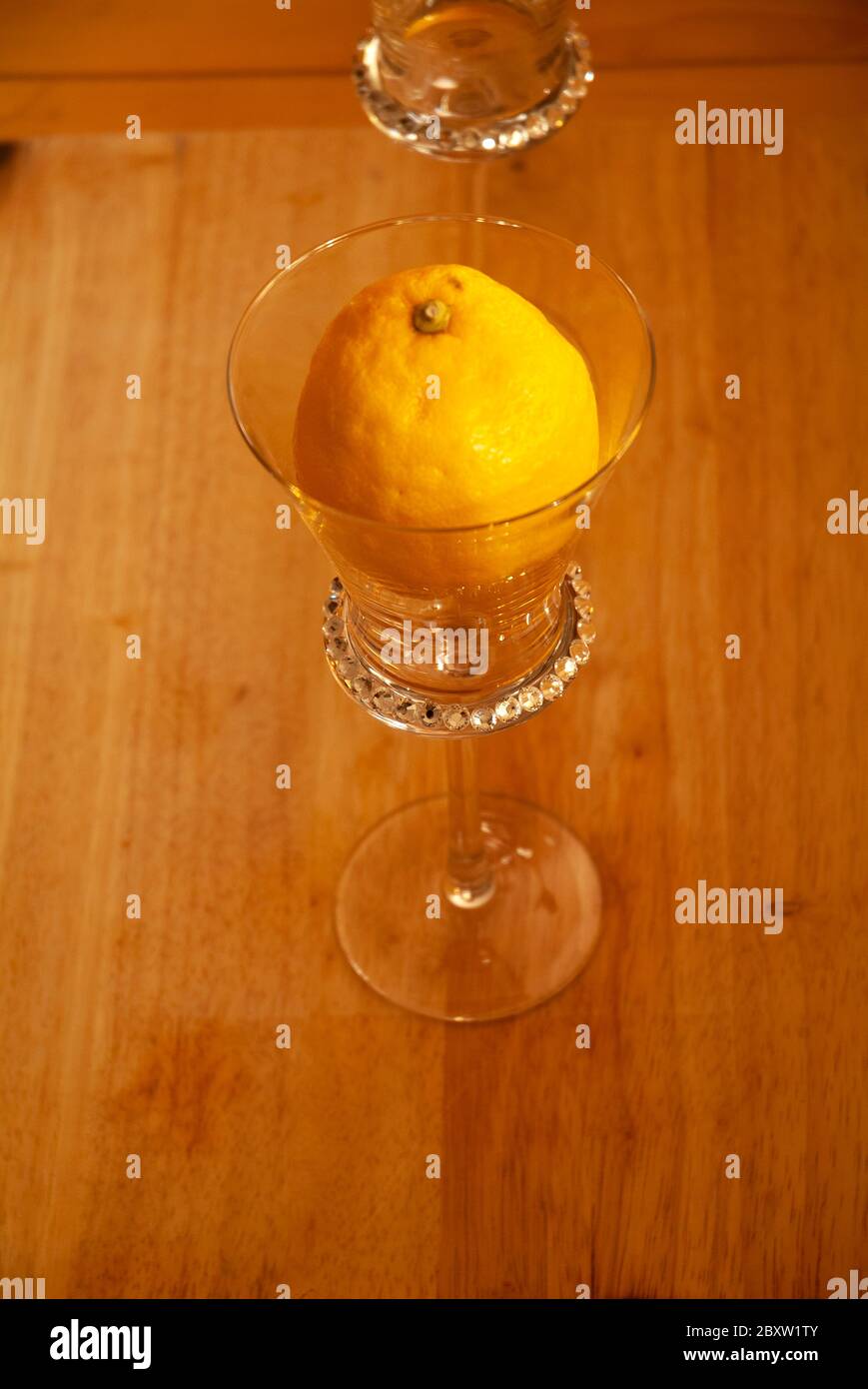 JUICE: A lemon and orange sit in wine glasses on a wooden cutting board. Stock Photo