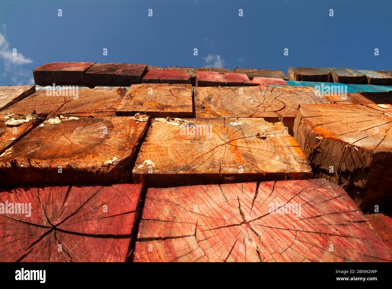TIMBER: Multicolored wooden logs are stacked into a wall in the parking lot of a shopping mall. Stock Photo
