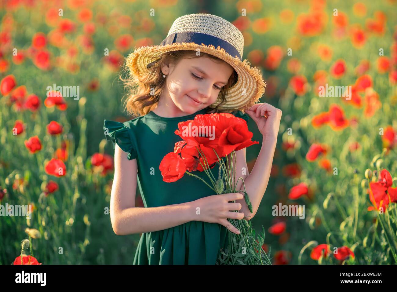Cute little girl in green dress and straw hat with a bouquet of poppies ...