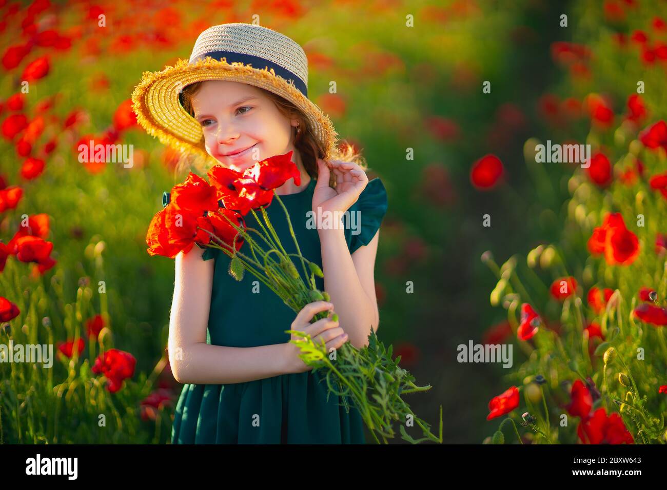 Cute little girl in green dress and straw hat with a bouquet of poppies ...
