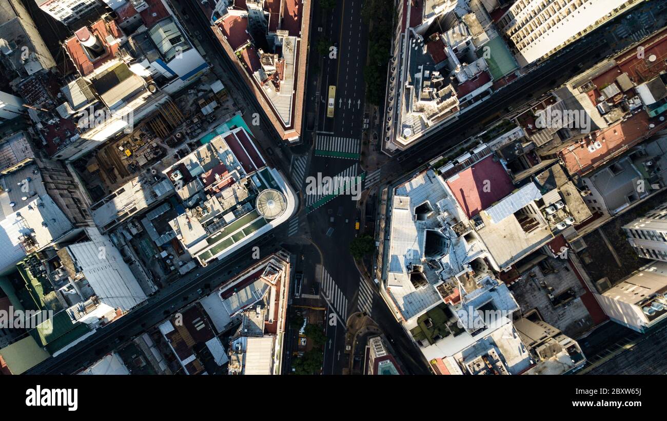 Aerial top-down view on a four-way intersection in between tall buildings during sunset time with no people or traffic due to quarantine 2020 Stock Photo