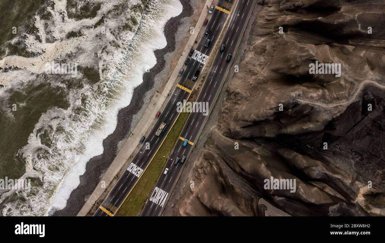 Aerial photo of the highway next to the Pacific Ocean in Lima, Peru, in between crashing waves and brown cliffs. Stock Photo