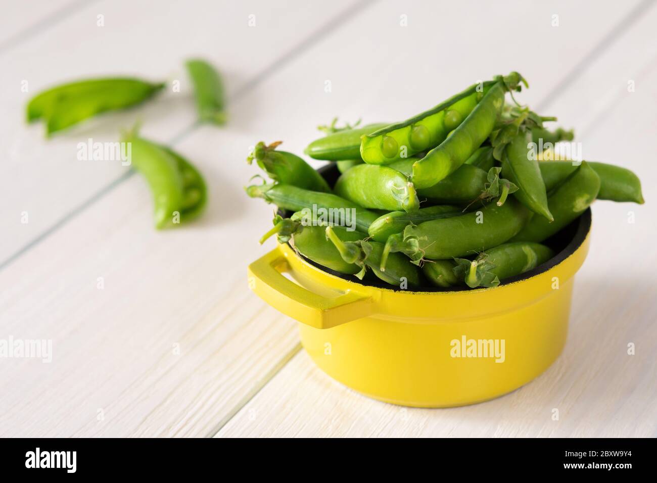 Fresh young green peas in pods in a yellow iron bowl, ripe organic