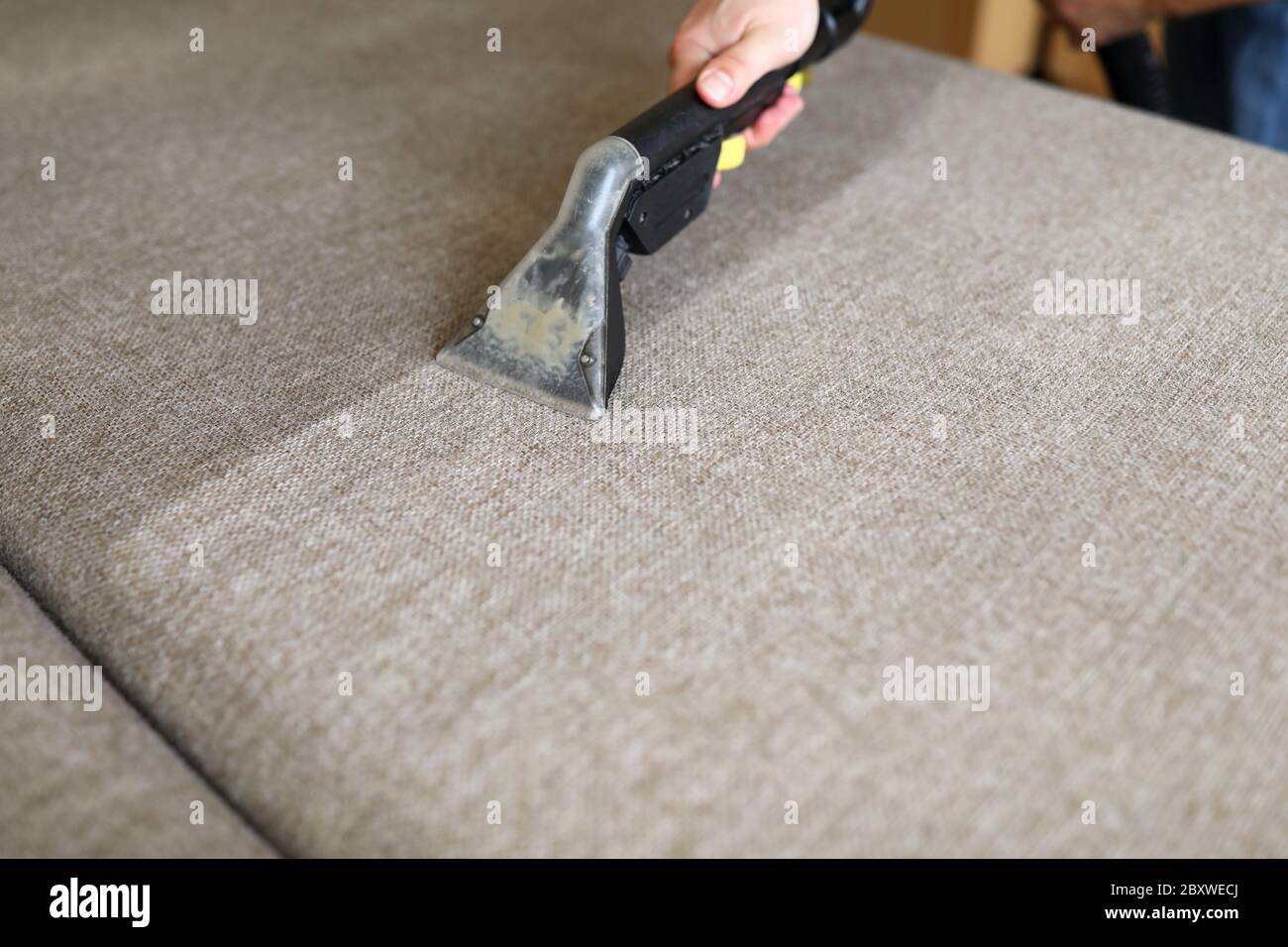 Male housekeeper arm cleaning sofa with washing vacuum cleaner Stock