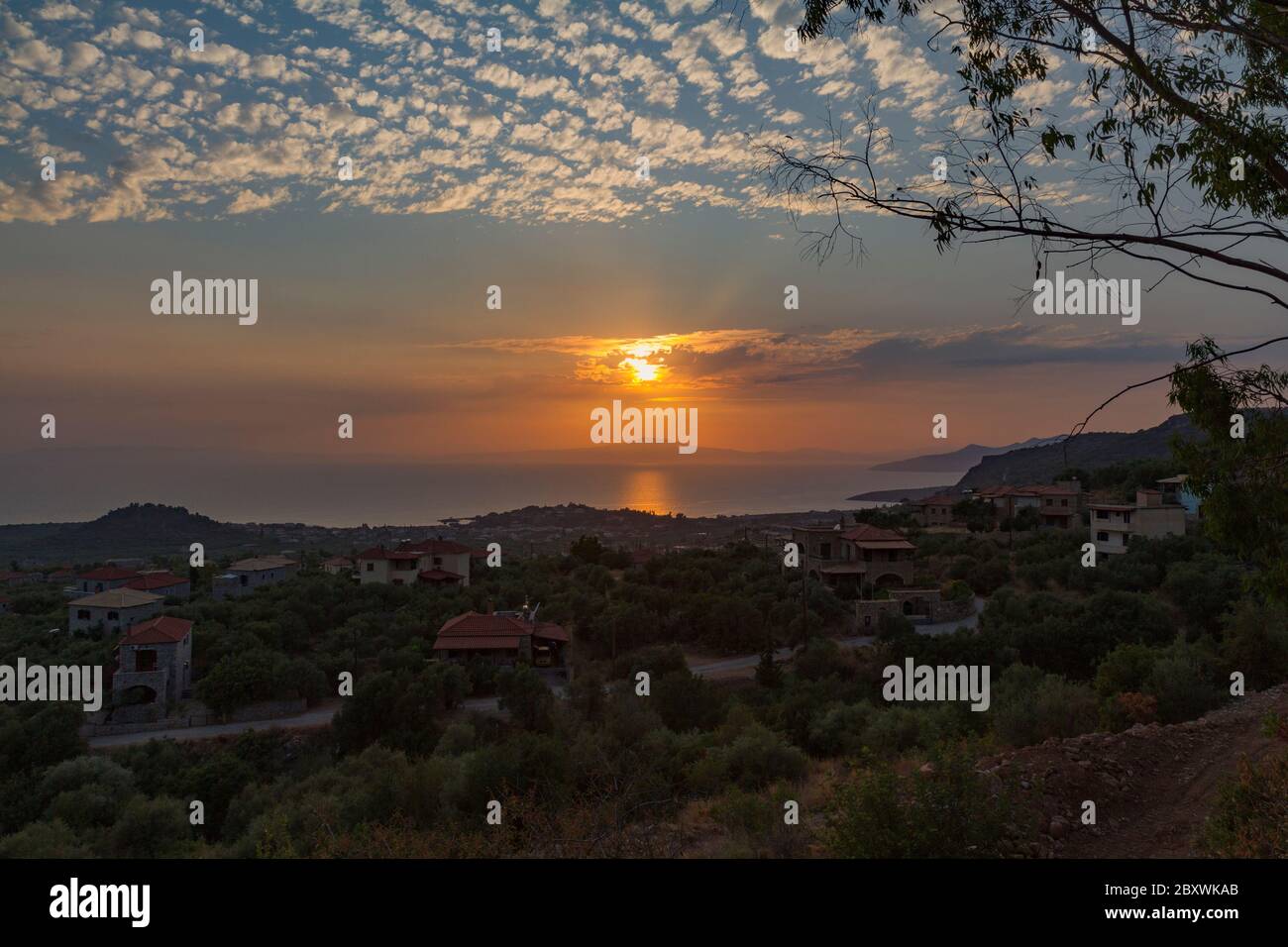 Sunset at village Stoupa, Messinia, Greece. A panoramic photo taken from a hill. The sun between light clouds, lighting the sea before setting. Stock Photo