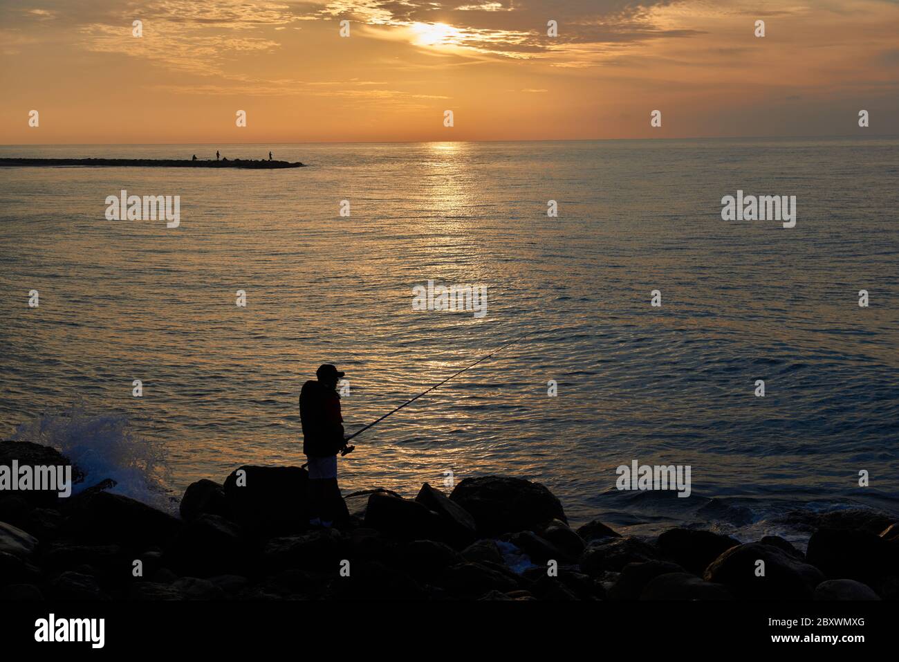 A silhouette of a fisherman on the beach in front of a spectacular ...