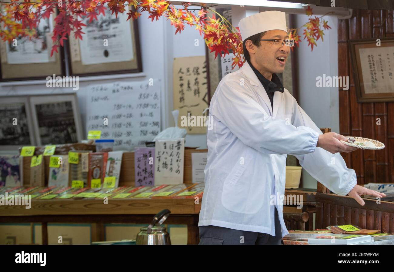 A chef offers passerby samples  of green tea - matcha, cakes, biscuits, candies and other confections. Matsubara Dori Kyoto, Japan. He Stock Photo