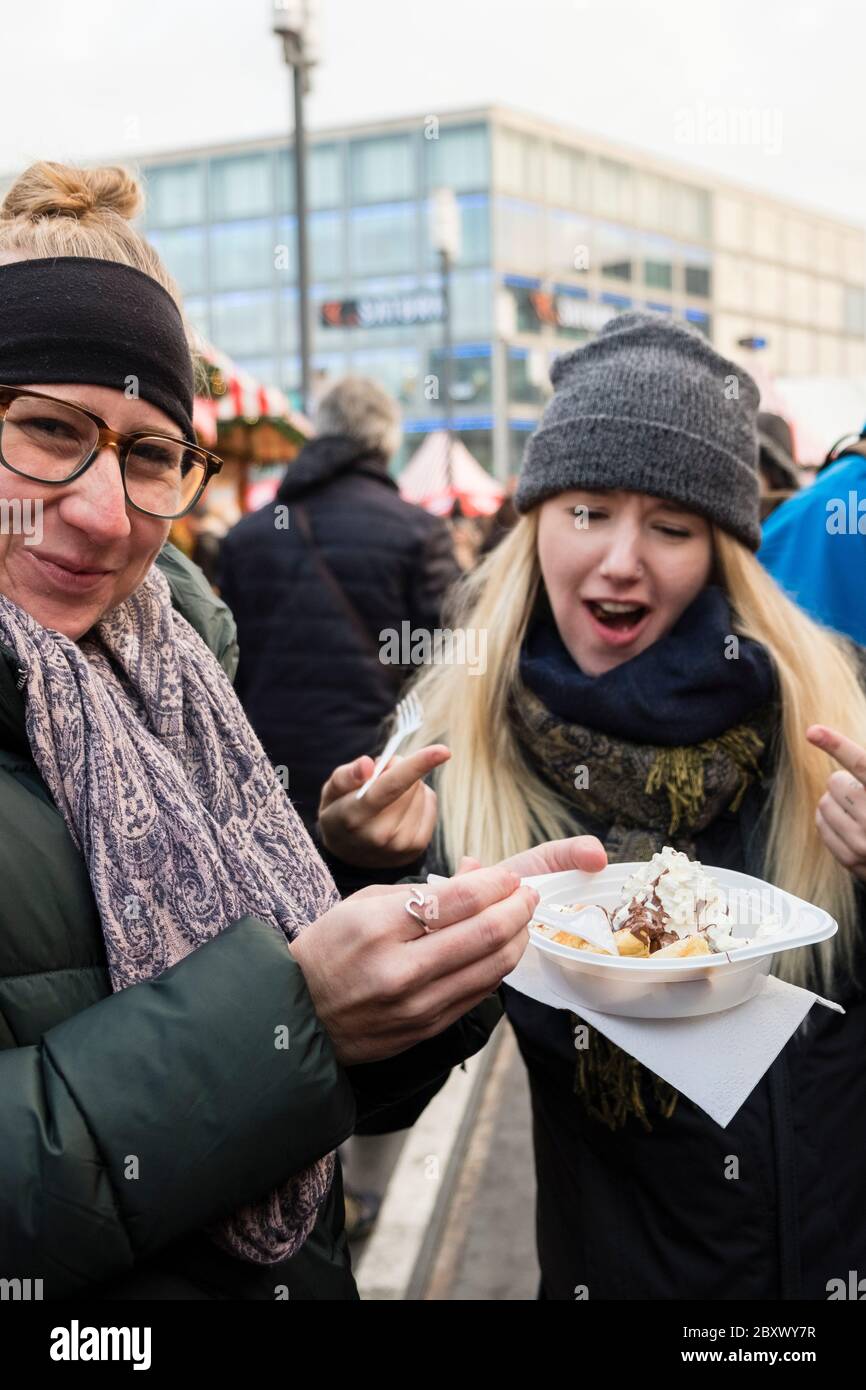 Two female tourists share a sweet gooey dessert from an outdoor food