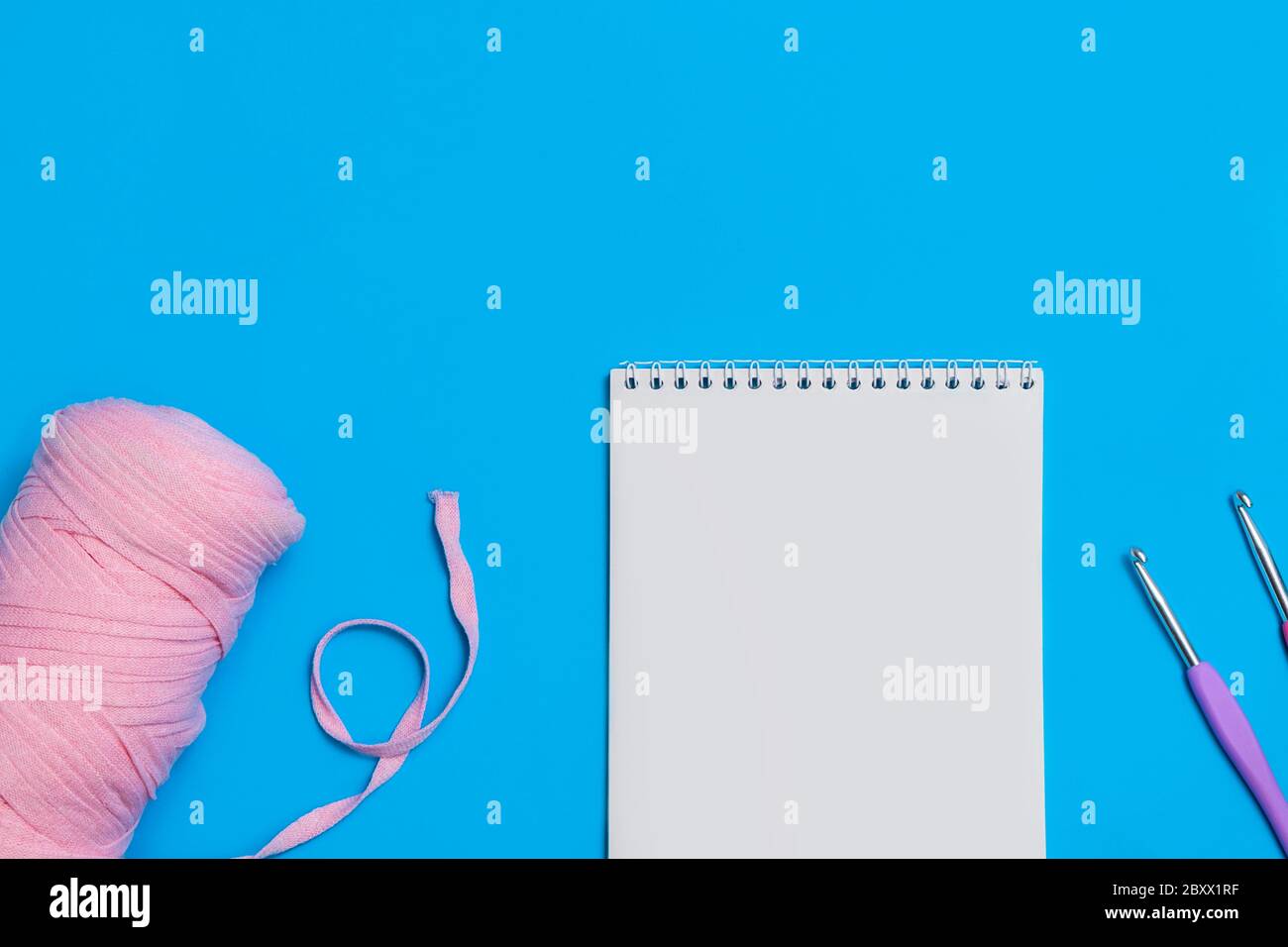 Top view of empty paper notepad with yarn and crochet hooks on blue background. Crocheting and hobby concept Stock Photo