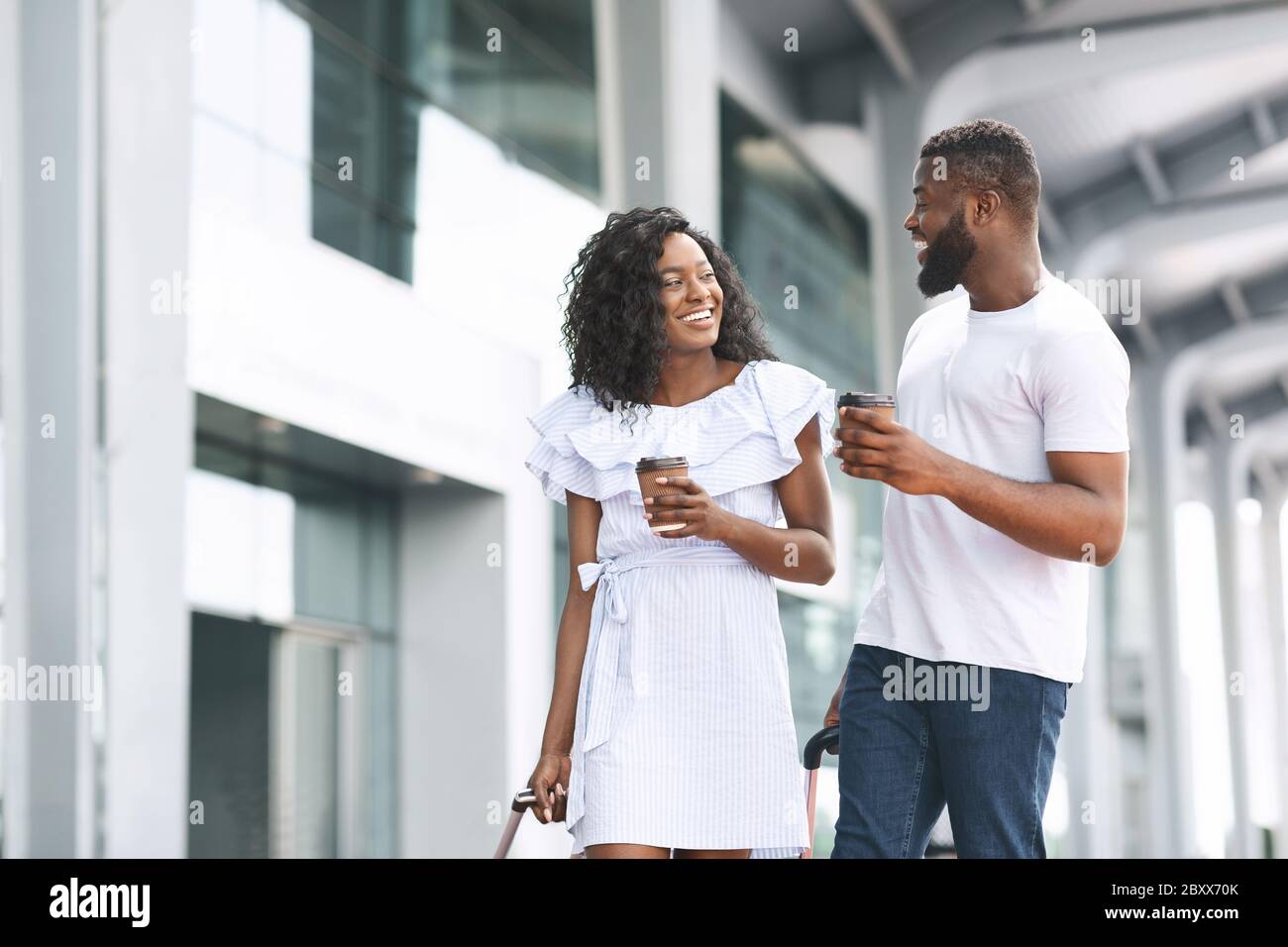 Happy Black Man And Woman Walking With Coffee Near Airport Building