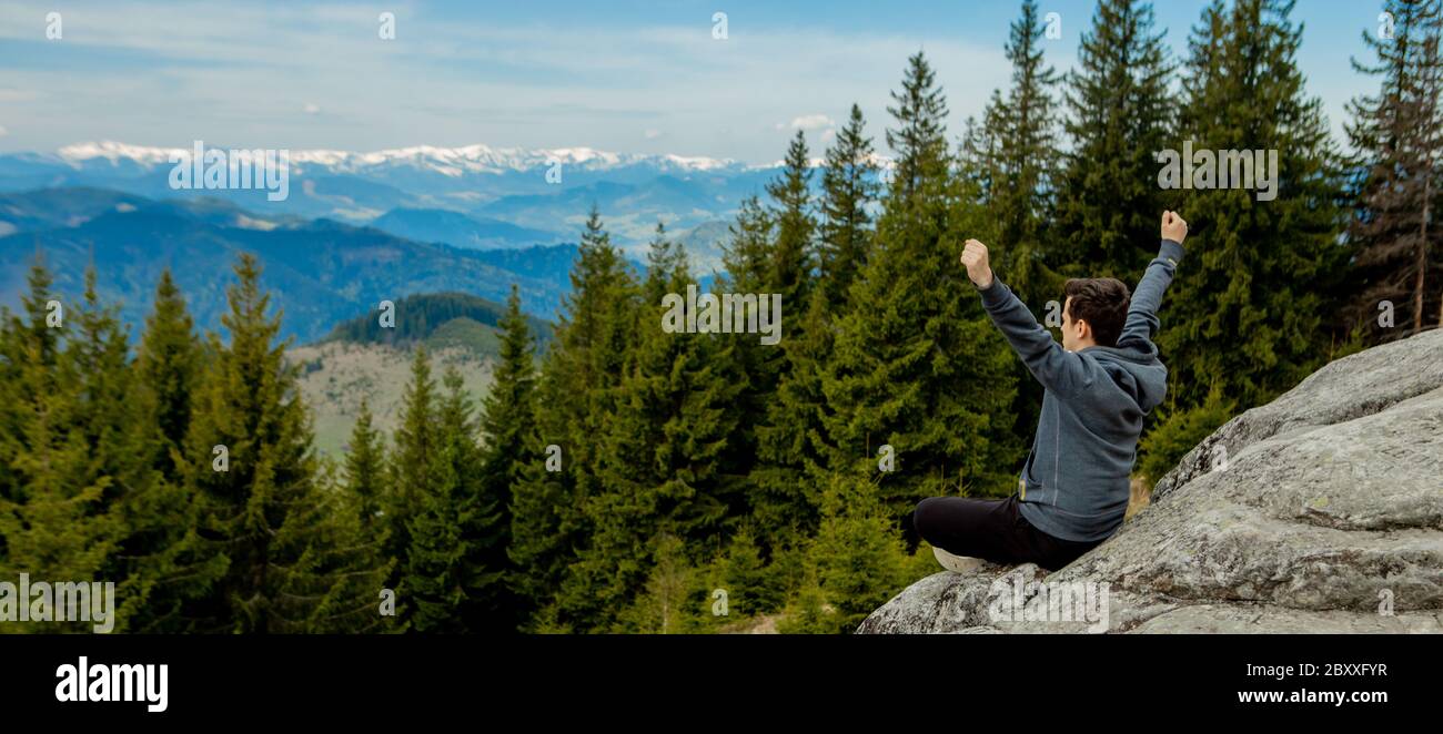 A man is high in the mountains against the sky, celebrating the victory, raising his hands up. Stock Photo