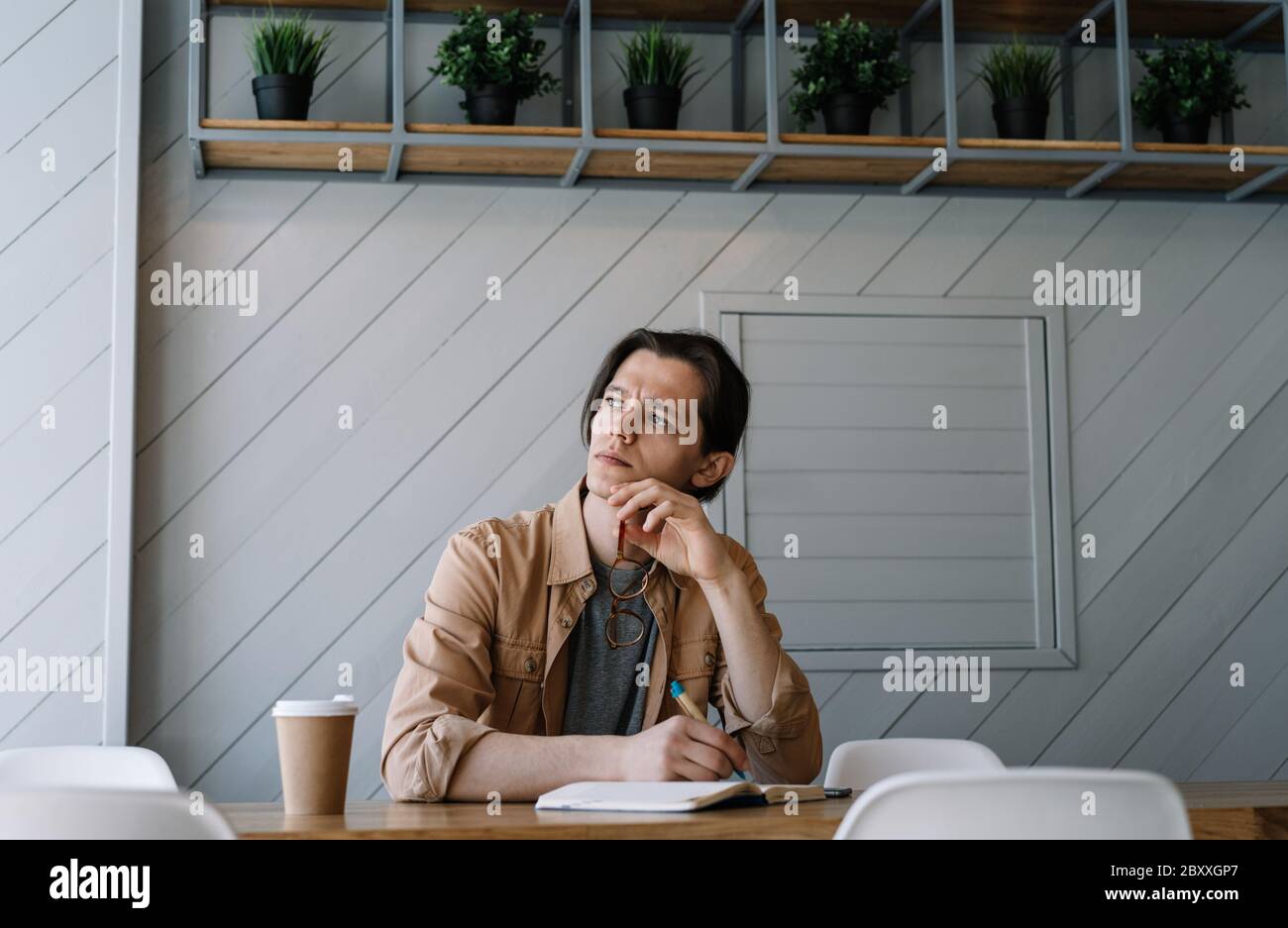 Serious man working freelance project, writing notes, thinking, brainstorming at workplace. Portrait of pensive student studying, learning language Stock Photo