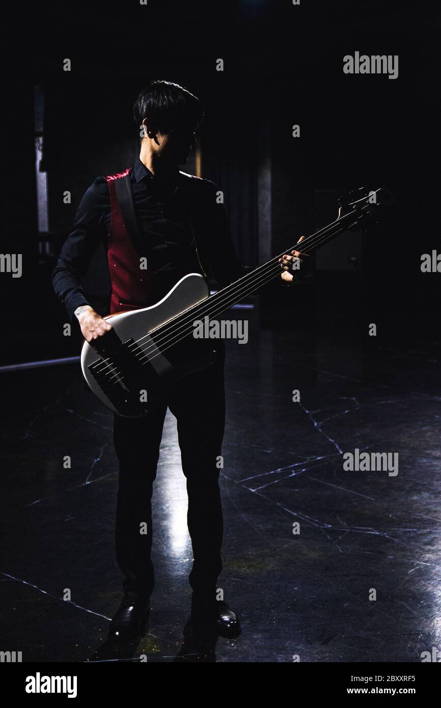 Bass guitar player in black clothes and red gillette in dark hall