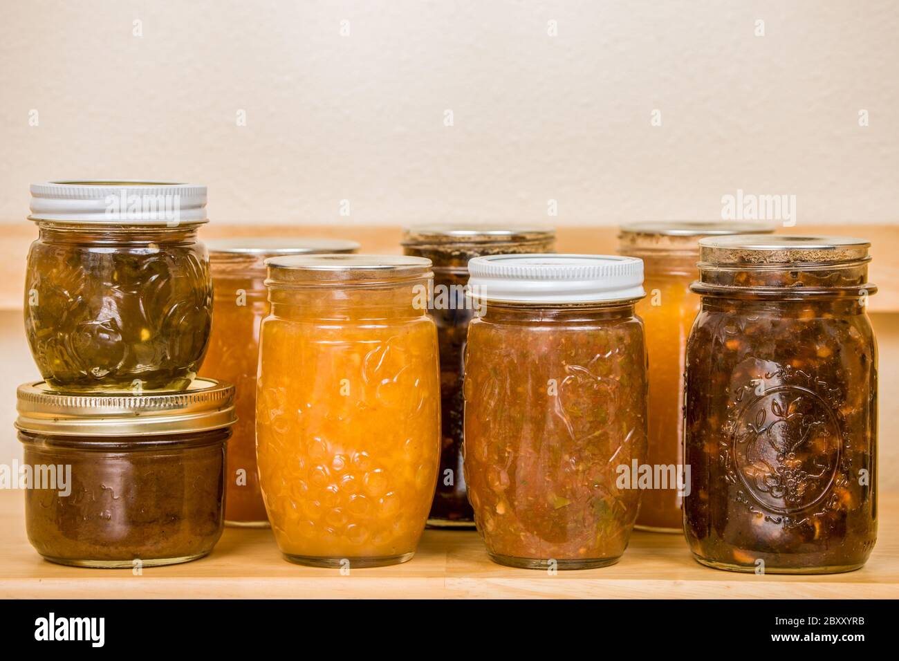 Homecanned goods on a pantry shelf, from left to right pepper jelly on top of pear butter