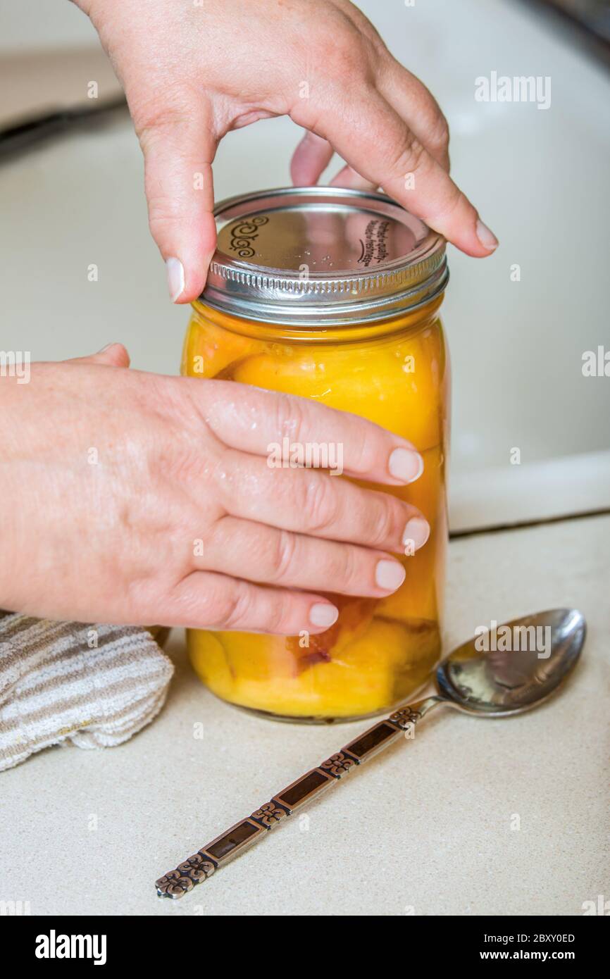 Woman screwing on a canning jar ring finger tight over a jar lid.  It is important to not over tighten the lid. Stock Photo