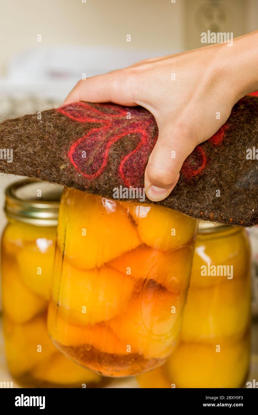 Woman removing jars of canned peaches from a hot water bath canner and