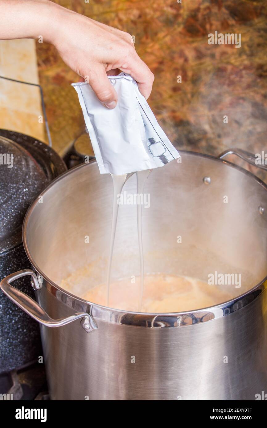 Woman adding a package of fruit pectin to boiling apricot jam.  Pectin is a natural fibre found in plant cell walls and most concentrated in the skin Stock Photo