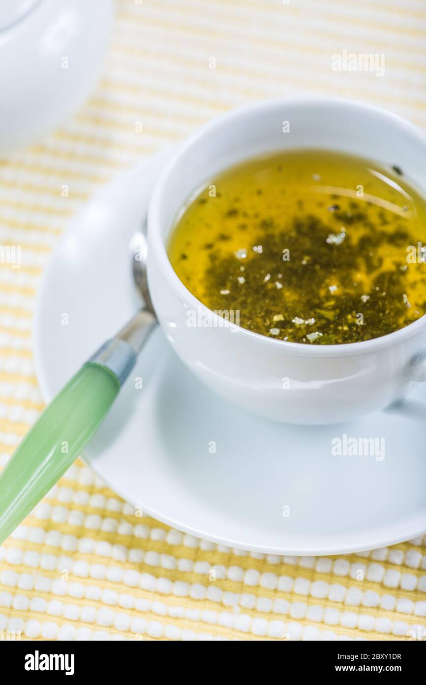 White ceramic cup of Sen-cha green tea, with the leaves seeping, and a spoon on the saucer Stock Photo