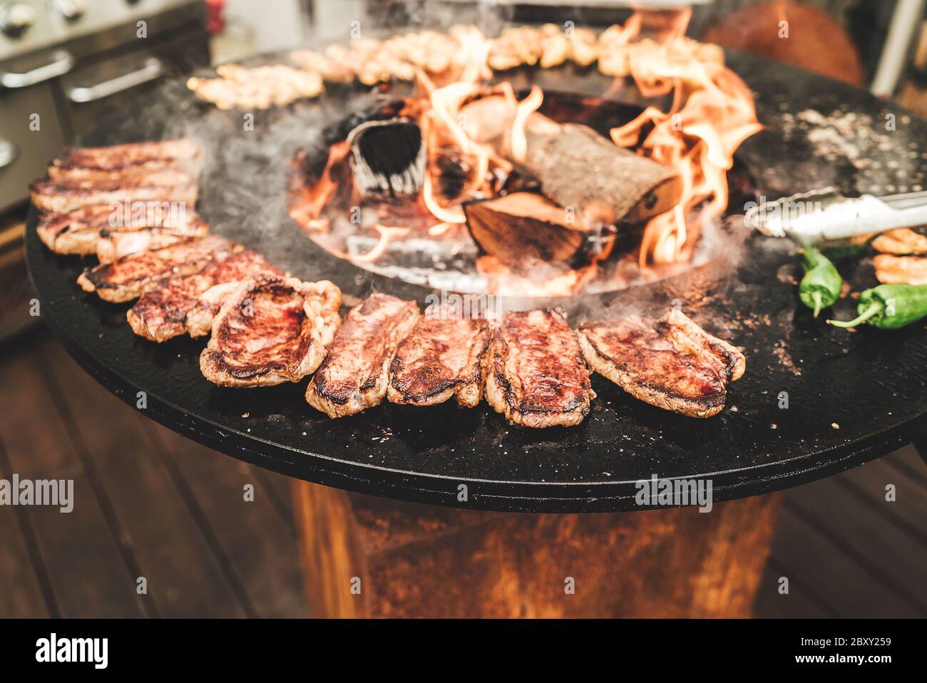 Round barbecue grill with open fire inside. Preparing steaks, shrimps and  green peppers. Party, BBQ, cooking and restaurant concept Stock Photo -  Alamy