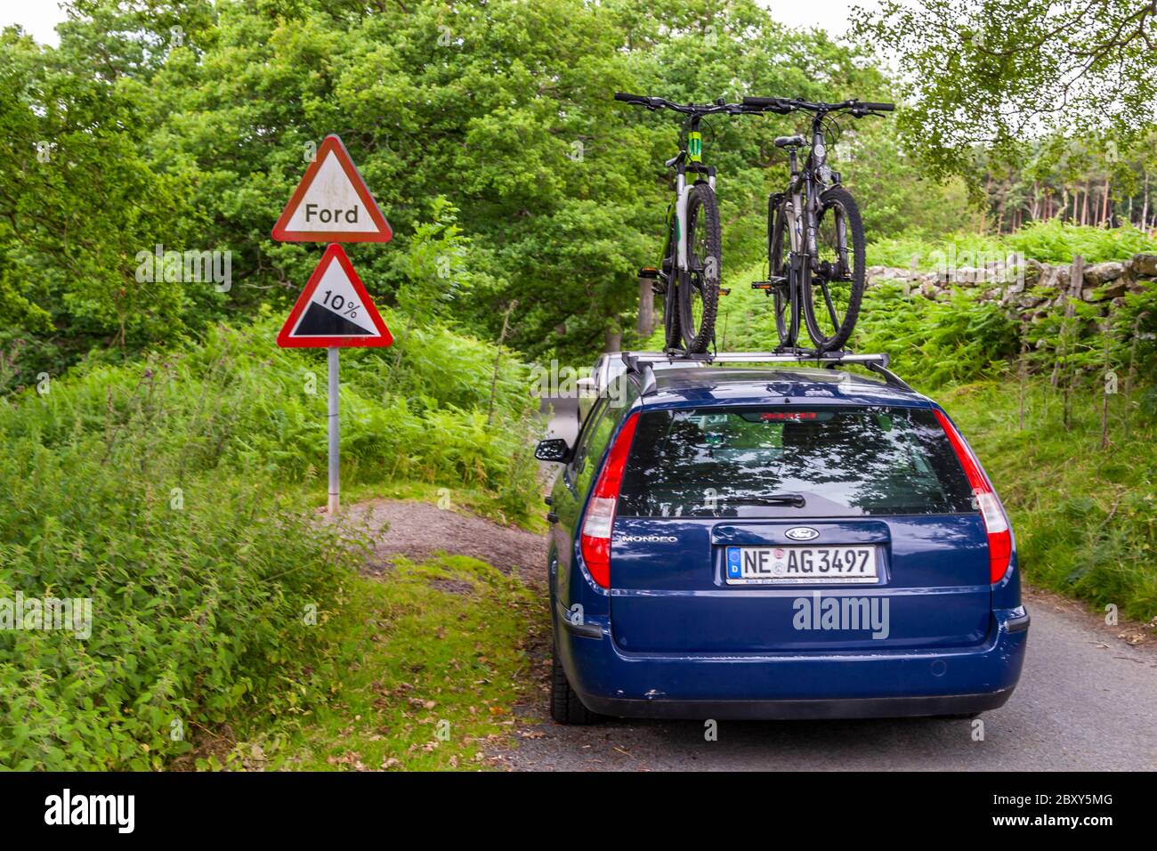 A Ford Mondeo with bicycles on the roof rack at a traffic sign 10 percent slope and ford Stock Photo