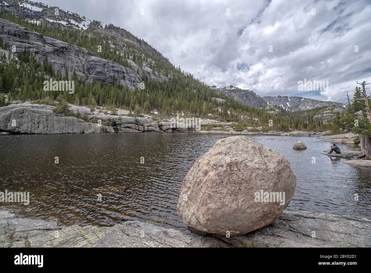 Mill's Pond Alpine Lake in Rocky Mountain National Park with a Rock, Tree, or Deadfall in the Foreground and Clouds and Mountains in the Background Stock Photo