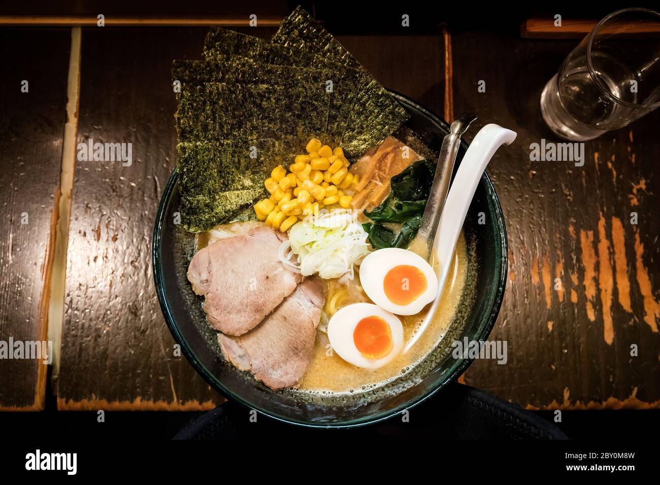 A bowl of ramen noodles with pork, egg and nori sheets on a typical wooden counter in a traditional Tokyo restaurant Stock Photo