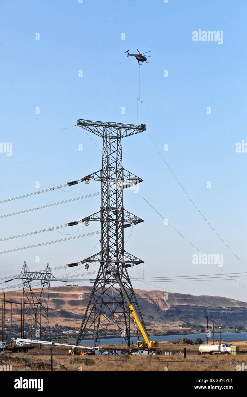 Helicopter flying sock line, threading the needle for the center phase, triple bundle travelers, electical transmission tower.  Hughes 500  helicopter. Stock Photo