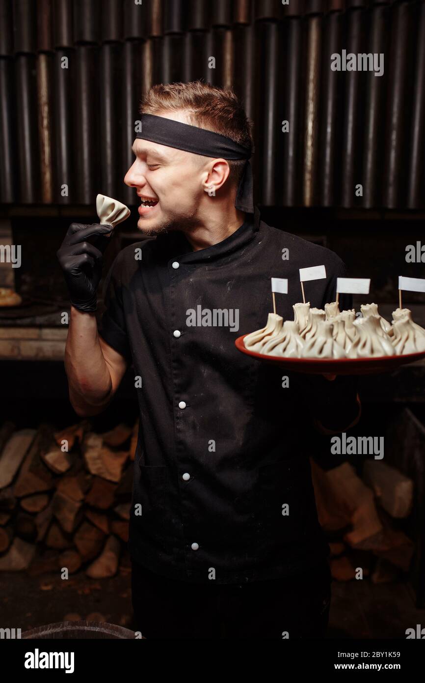 Cheerful chef posing with a serving of Khinkali. Georgian national traditional cuisine. Cooking process. Kitchen. Food concept Stock Photo