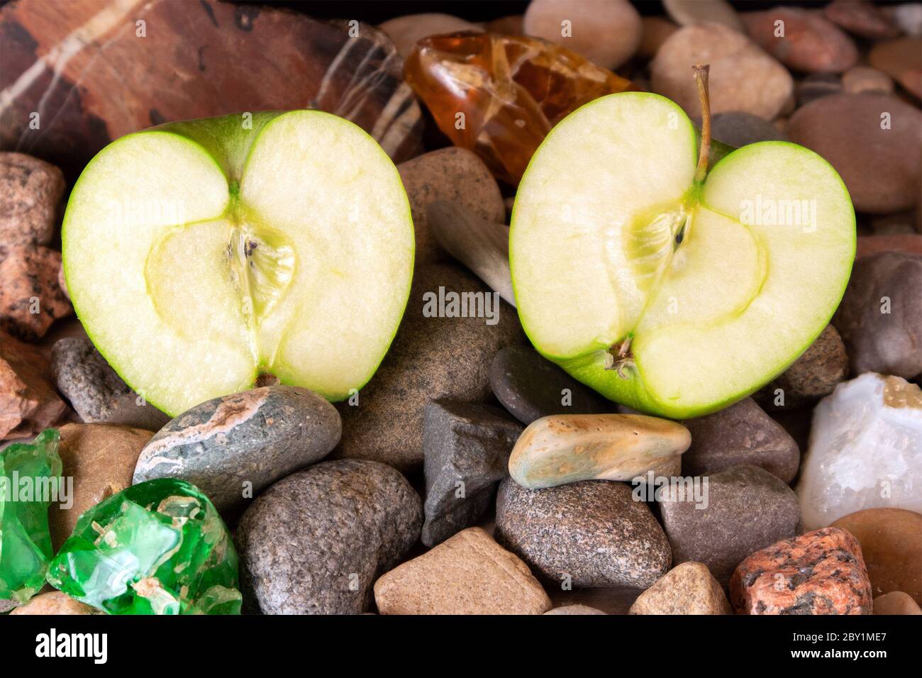 Halves of big green apple lying on pebble decorated with agate, jasper and colored glass Stock Photo