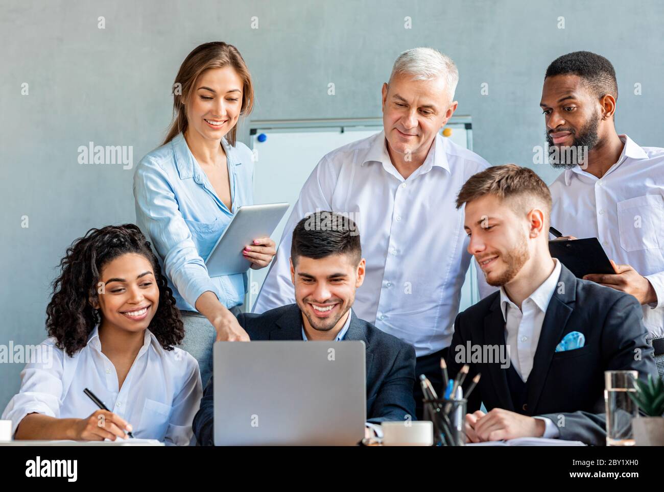 Smiling Coworkers Working Together On One Laptop In Modern Office Stock Photo