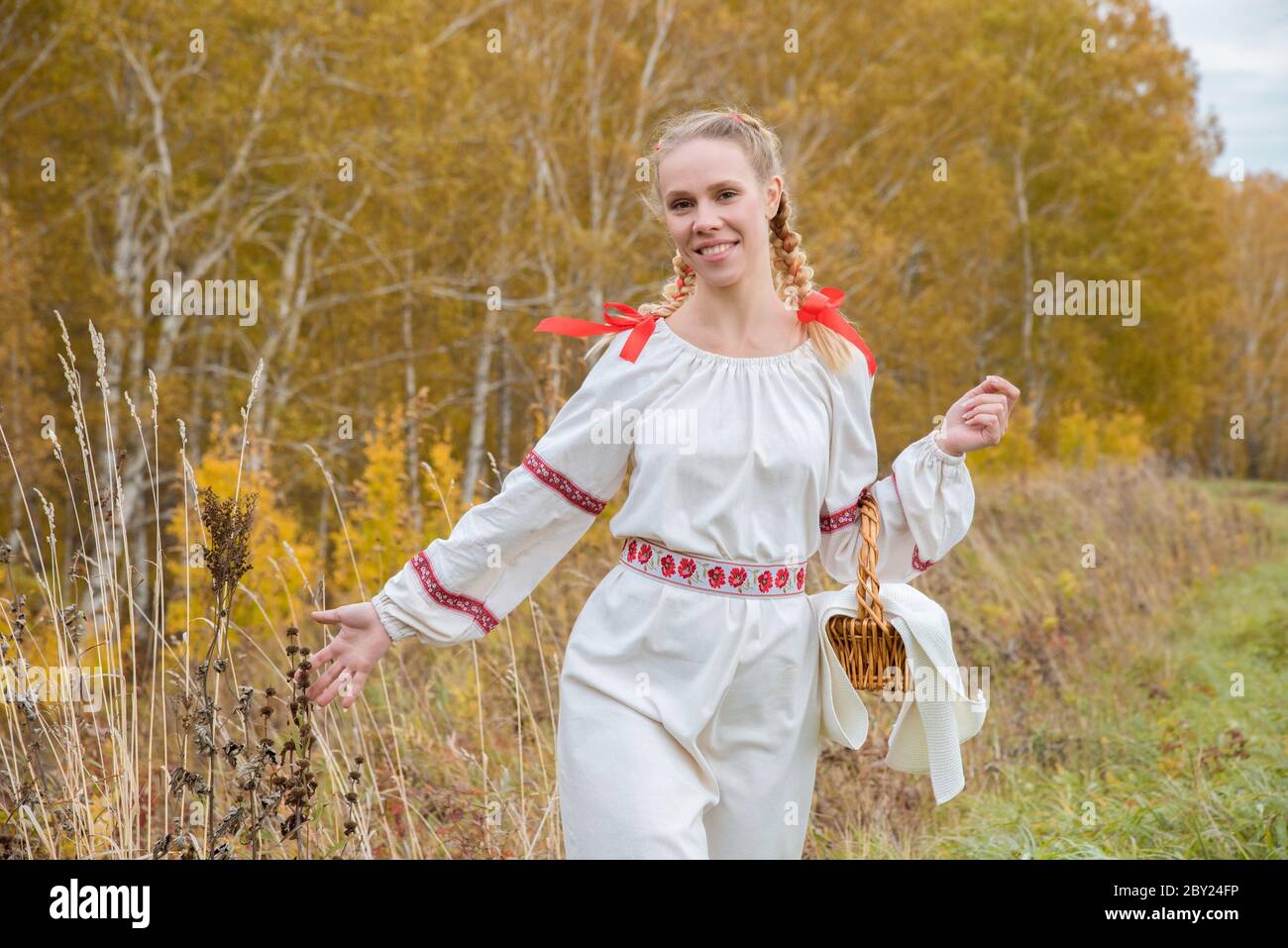 Beautiful blonde girl in a traditional Slavic dress with a straw basket ...