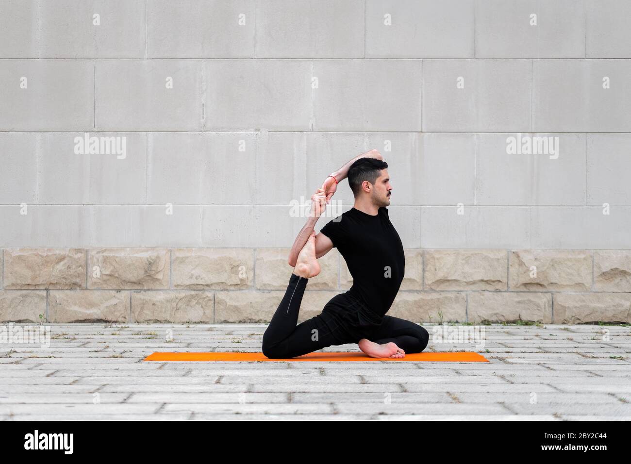 Handsome sporty latin man exercising in a city, doing yoga, fitness or pilates training, One Legged King Pigeon Pose. Stock Photo