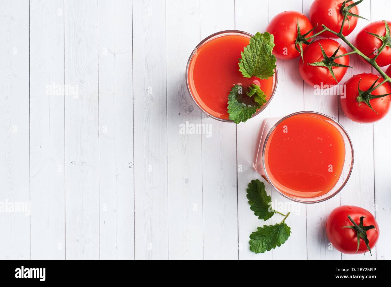 Tomato juice in glass glasses and fresh ripe tomatoes on a branch. White wooden background with copy space Stock Photo