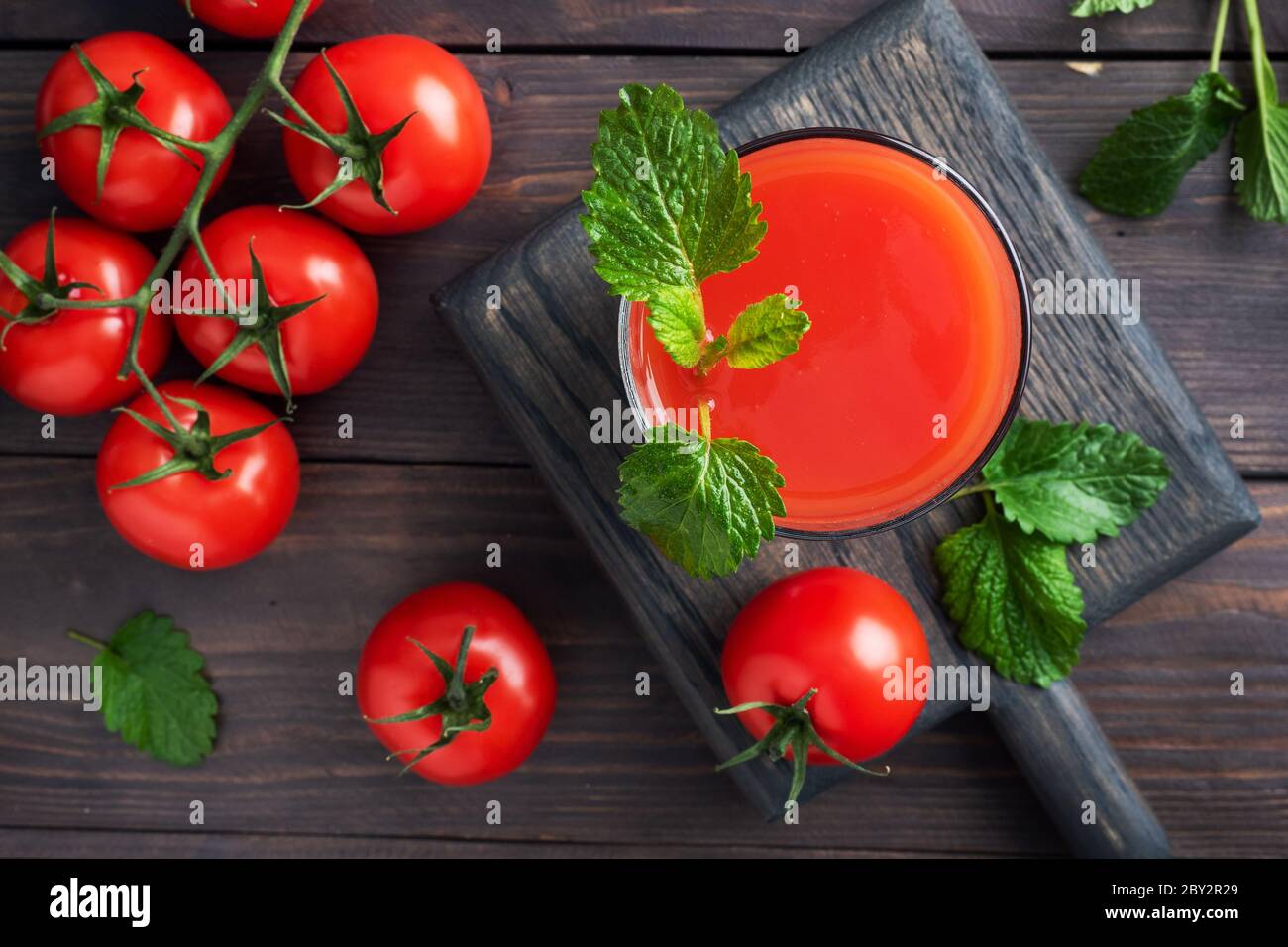 Tomato juice in glass glasses and fresh ripe tomatoes on a branch. Dark wooden background with copy space Stock Photo