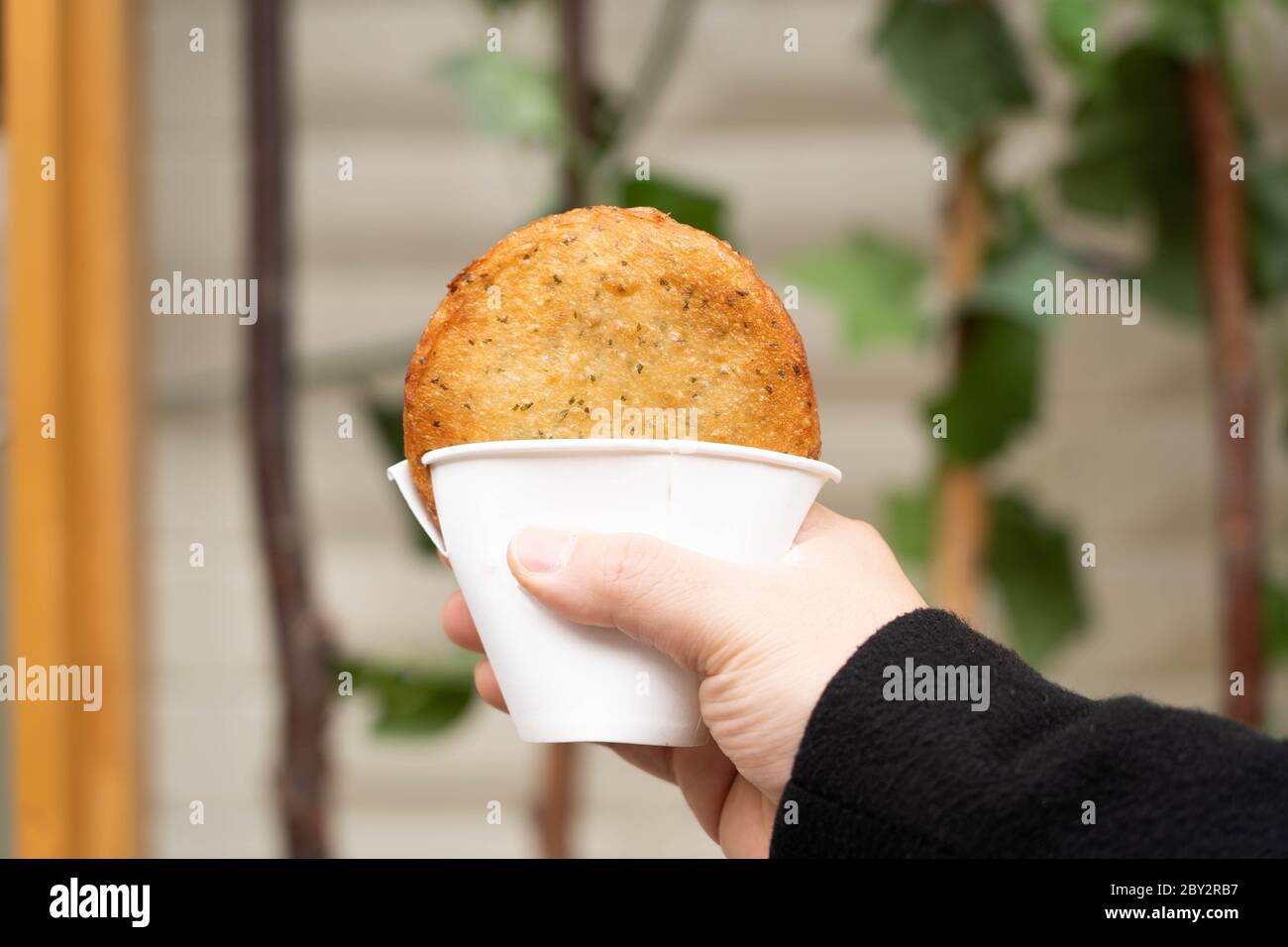 Hand holding a Korean traditional street food, deep fried pancake, Hotteok, with sweet fillings in a cup. Stock Photo